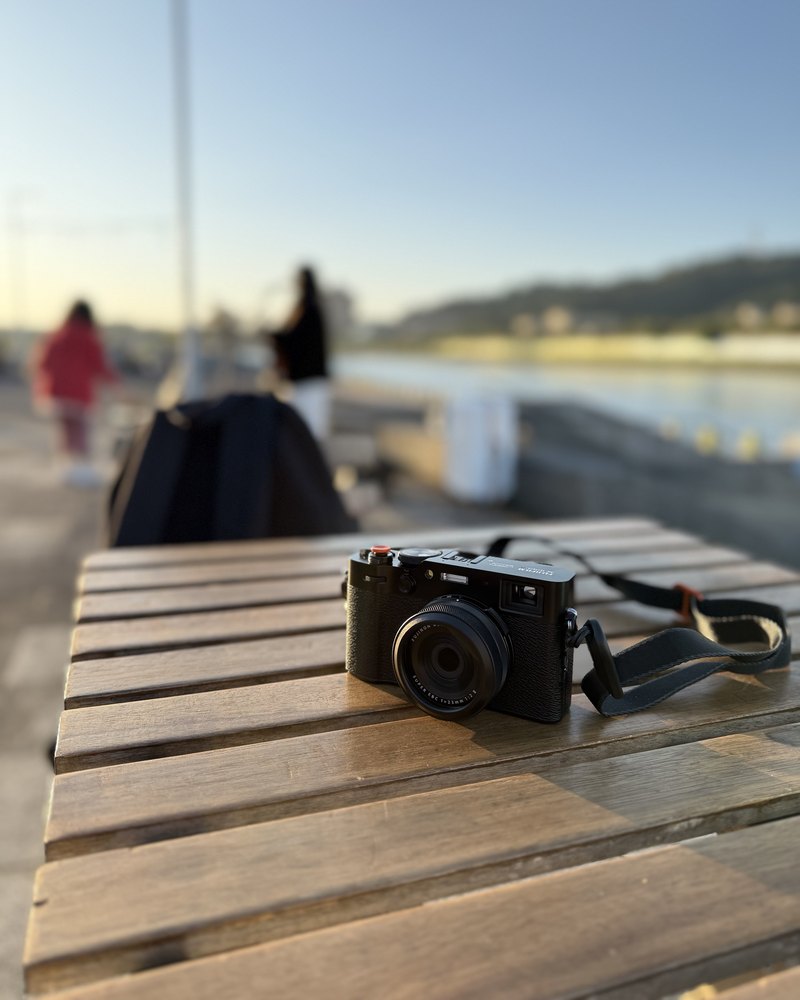 A compact camera on a wooden table by the water